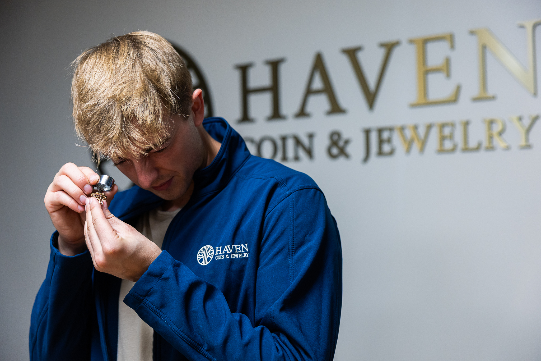 A young man using a jeweler's loop to look at a piece of jewelry.