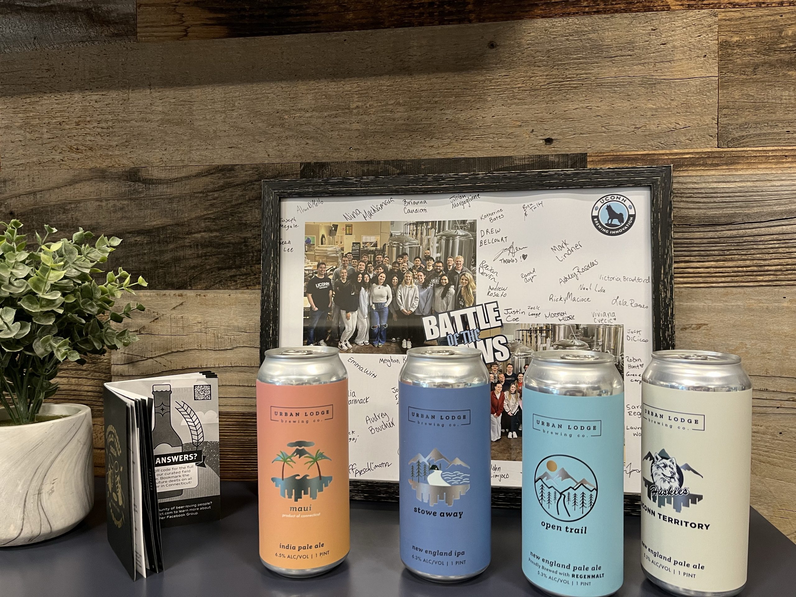 Urban Lodge beers lined up in front of a picture from the Battle of the Brews.
